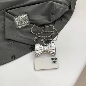 Detalle de bolso mariposa plateado espejo con cadena y teléfono para escala de tamaño