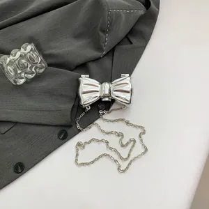Detalle de bolso de fiesta mariposa plateado con acabado espejo y correa de cadena fina