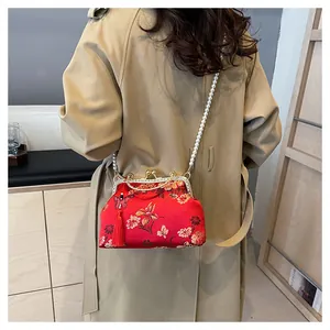 Vue détaillée du sac brodé rouge avec perles et pompon sur un trench-coat beige