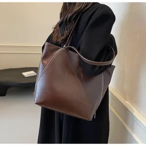 Detail of a large dark brown faux leather tote bag with glossy finish and side zippers