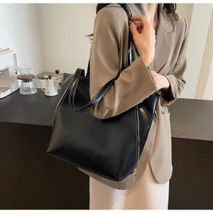 Close-up of black tote bag featuring contrast white stitching and silver metal zippers