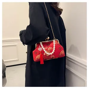 Detalle de bordado de flores doradas en bolso de satén rojo con asa de perlas