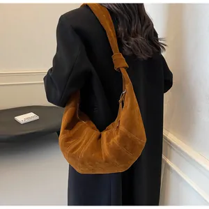 Detail of caramel suede crossbody bag with knotted shoulder strap on a black coat
