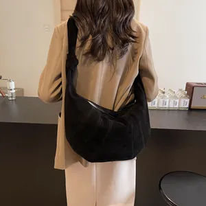 Large black suede crescent bag with knot detail shown on a model in a minimalist setting