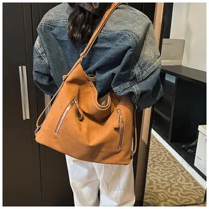 Sac hobo en daim marron caramel avec fermetures éclair argentées porté à l'épaule