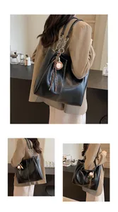 Detalle de bolso tote minimalista de cuero negro con costuras blancas y asa de cadena