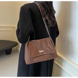 Detail of a shiny brown lacquer shoulder bag with silver metal plaque and chain strap