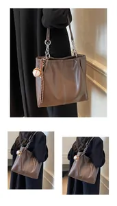Detalle de bolso tote marrón con costuras verticales y colgante de béisbol de moda