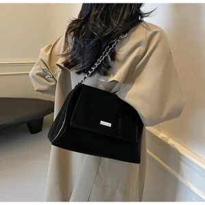 Detail of black leather shoulder bag with chain strap worn with beige trench coat