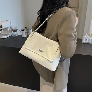 Fashionable cream white patent leather underarm bag with silver chain strap worn by a model