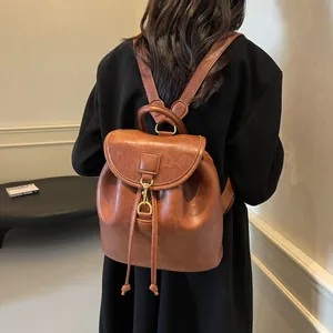 Detail of a brown leather backpack with drawstring closure and gold metallic buckles