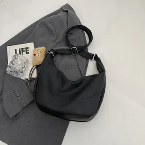 Detail of black lychee texture crescent bag on a grey blazer with silver hardware