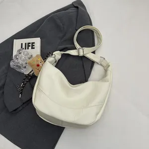 White faux leather crescent bag with adjustable strap and bear charm on blazer background