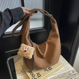 Detail of caramel crescent shoulder bag with pebbled leather texture and plush charm