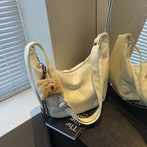 Macro shot of cream hobo bag with pebble leather texture and cute plush charm pendant