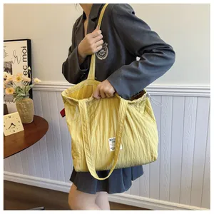 Detail view of yellow pleated nylon tote bag featuring a drawstring and white woven label