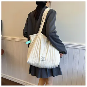 Detail of cream pleated tote bag featuring woven brand label and textured fabric finish