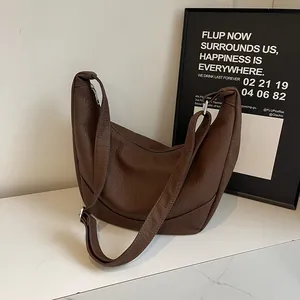 Detail of a brown textured faux leather hobo bag with wide strap on marble background