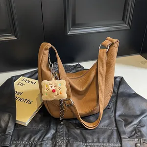 Detail of caramel half-moon bag with lychee texture and cute plush charm on leather jacket