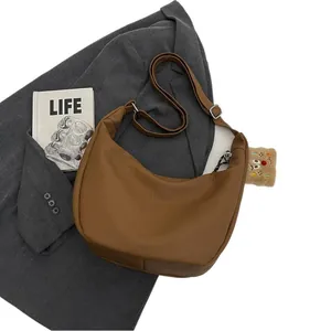 Brown litchi texture crescent hobo bag with teddy bear pendant on grey blazer background