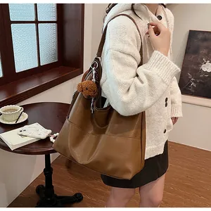 Close-up of brown leather tote bag featuring contrast stitching and a plush bear charm