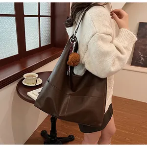 Detail of dark brown leather tote bag with plush bear charm in a cozy cafe setting