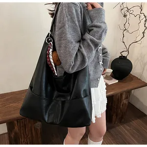 Black tote bag detail with plaid scarf, plush bear charm, and side pocket on the shoulder