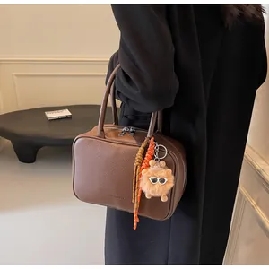 Detail der dunkelbraunen Lederhandtasche mit geprägtem Logo und dekorativem Anhänger