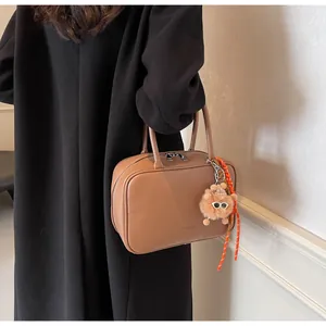 Detail der braunen Handtasche aus genarbtem Leder mit Plüsch-Anhänger und Logo
