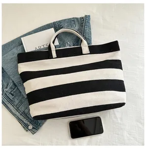 Overhead view of a black and white striped canvas tote bag with book and blue jeans
