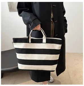 Detail of a large capacity black and white striped tote bag held by a model in a black coat