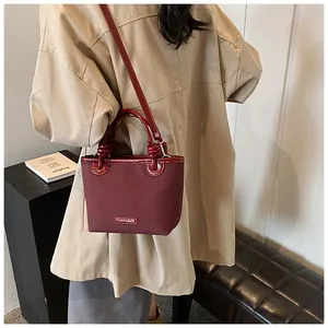 Detail der weinroten matten Beuteltasche mit Lackledergriffen und metallenem Markenlogo