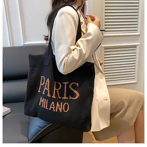Detalle del bolso tote de punto que muestra la tela negra con el texto naranja PARIS MILANO