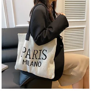 Detalle del bolso de punto con correas negras y texto Paris Milano en tejido crema