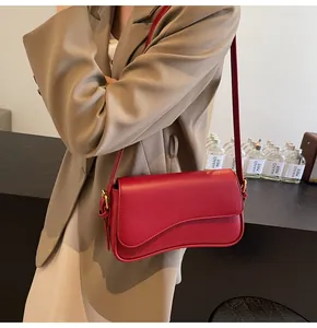 Close-up of a red litchi texture leather crossbody bag with asymmetric flap on a model