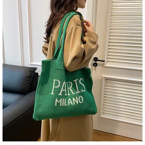 Detalle de bolso tote de punto verde con texto Paris Milano llevado en el hombro
