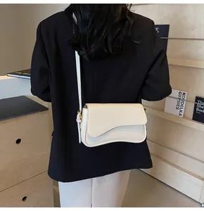 Detail of off-white textured leather crossbody bag with wave flap and gold hardware
