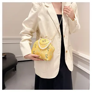 Detalle del bolso qipao de brocado amarillo con asa de perlas y cadena dorada