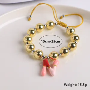 Detalle de pulsera tejida ajustable con cuentas doradas y colgante de letra N esmaltada