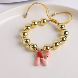 Detalle de pulsera de cuentas bañada en oro de 18K con colgante de letra N esmaltada