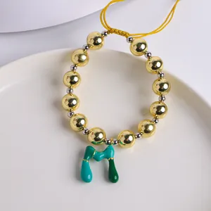 Detalle de pulsera de cuentas en oro 18K con colgante de letra M en esmalte verde