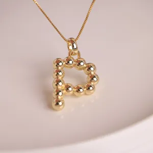 Macro detail of 18K gold plated letter P balloon pendant on a minimalist chain
