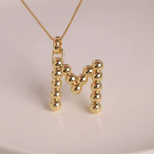Detailed view of an 18K gold-plated M letter pendant with unique beaded metal texture