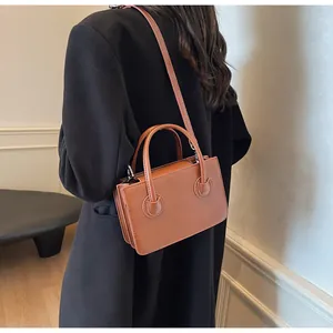 Borsa a tracolla in pelle color caramello con manici mostrata su un cappotto nero