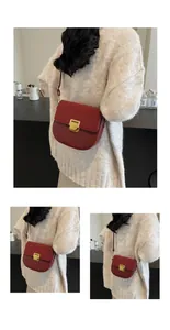 Dettaglio borsa a sella rosso scuro con trama scamosciata e fibbia oro su maglione crema