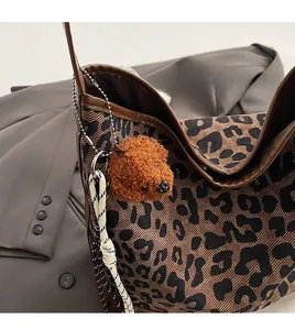 Detail of caramel plush teddy bear charm with braided rope on leopard print tote bag