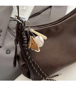 Dettaglio del ciondolo a tema baseball con guanto in pelle e mazza su borsa marrone