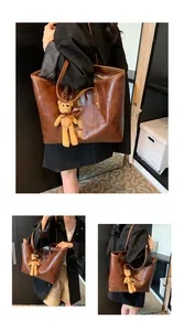Detail of a brown leather tote bag with geometric stitching and a yellow bear charm