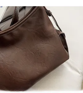 Dettaglio della texture in pelle vintage e cuciture bianche su una borsa a secchiello marrone