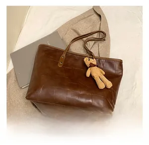 Detail view of large brown tote bag with retro leather texture and cute bear charm